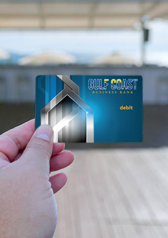 Gulf Coast Business Bank debit card being held up with a beach background